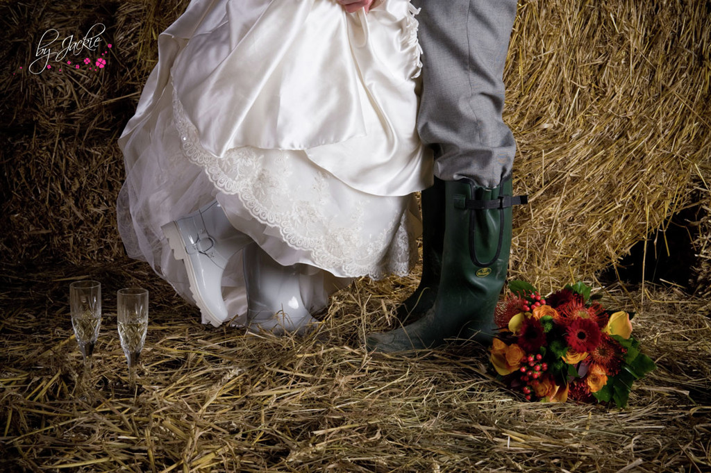 Photo of bride and groom wearing wellington boots in a barn in front of haystacks at a rural wedding in Selby, Yorkshire. Image copyright By Jackie Photography in Hemingbrough, Selby.