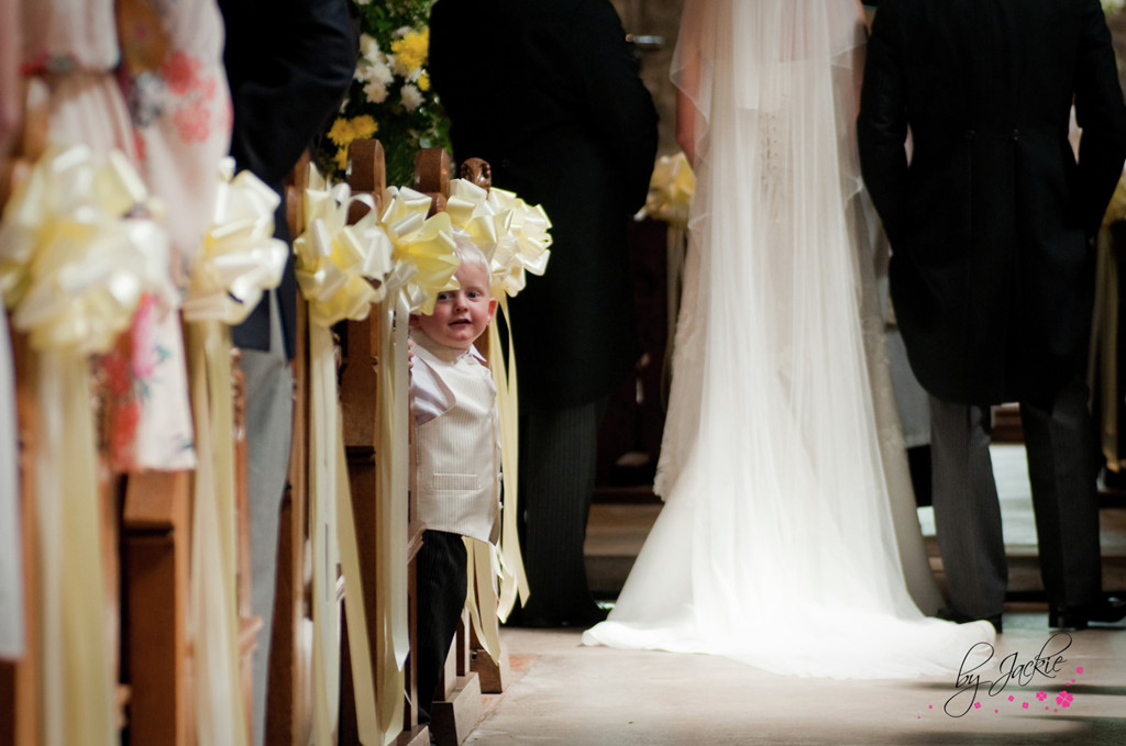 Photo of page boy peeping round the pew at a church wedding in Bubwith, near Howden. Image copyright By Jackie Photography in Selby