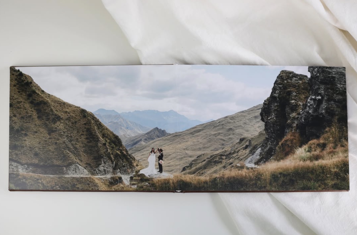 Open wedding album displaying a panoramic mountain portrait across a full spread.